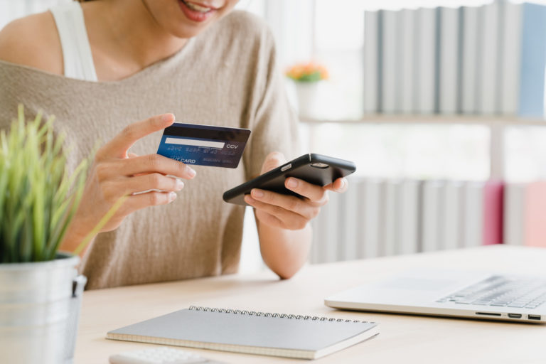 Woman using smartphone buying online shopping by credit card while wear sweater sitting on desk in living room at home